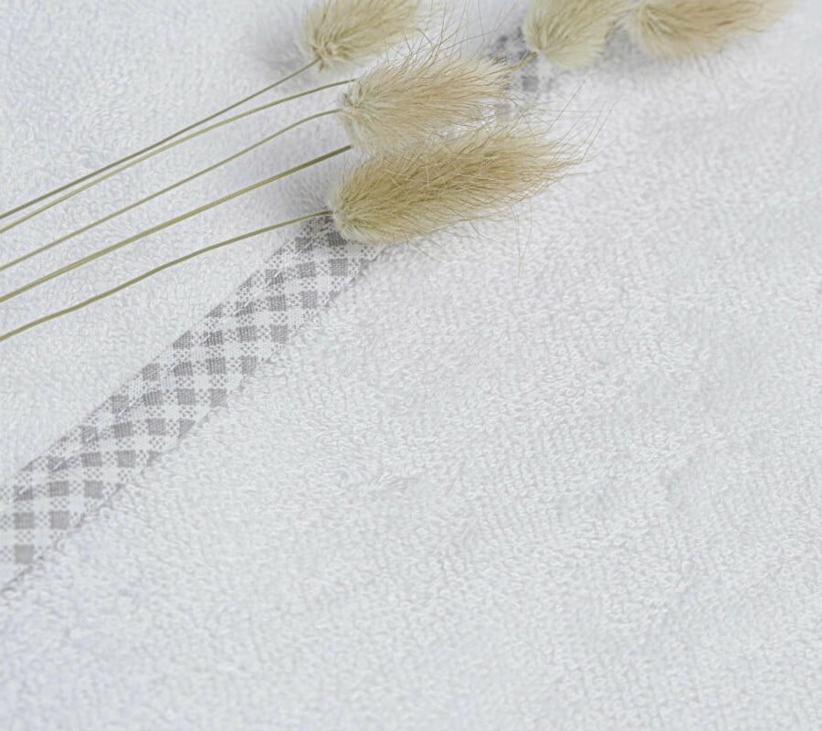 Détail sortie de bain en éponge pour bébé blanche avec un liseré en vichy gris avec des fleurs de pampa