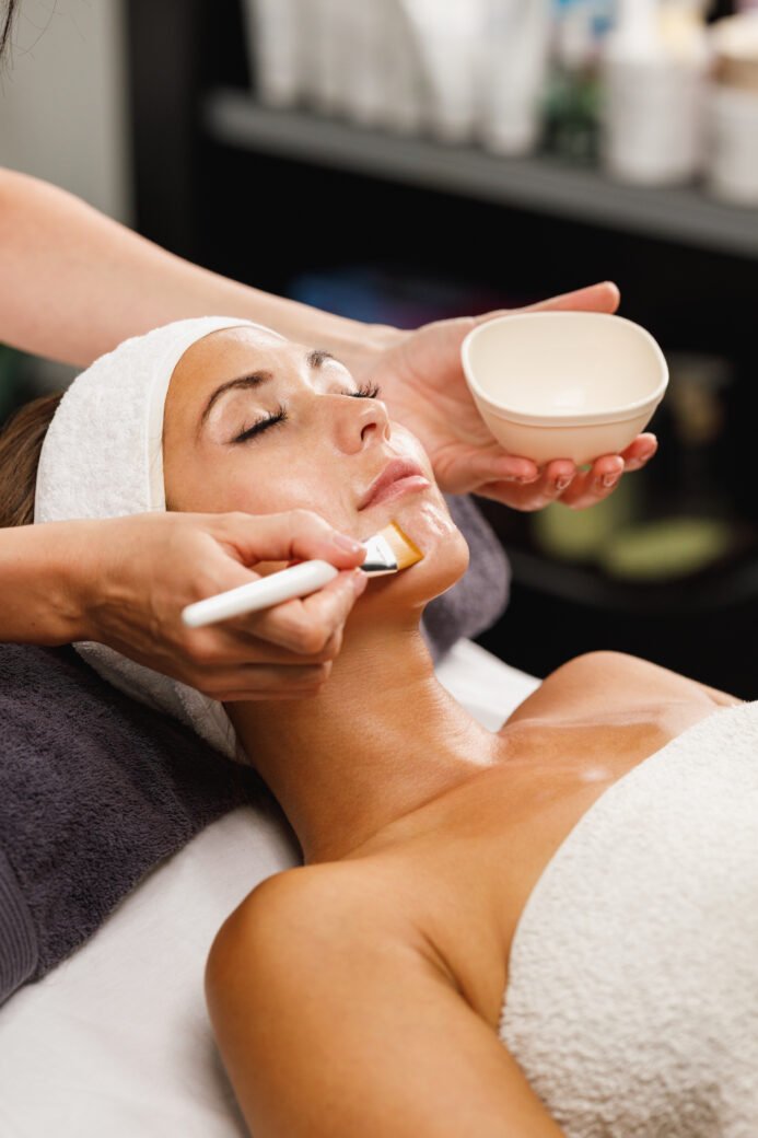 Une cliente s'offre un moment de détente et de bien-être pendant un soin de beauté. Les mains expertes du professionnel travaillent avec attention pour procurer une expérience relaxante et apaisante. L'image capture l'essence de la quiétude dans un environnement dédié à l'épanouissement et à la beauté personnelle. Le linge Comptoir du bambou participe avec style à son confort et à la protection de la planète.